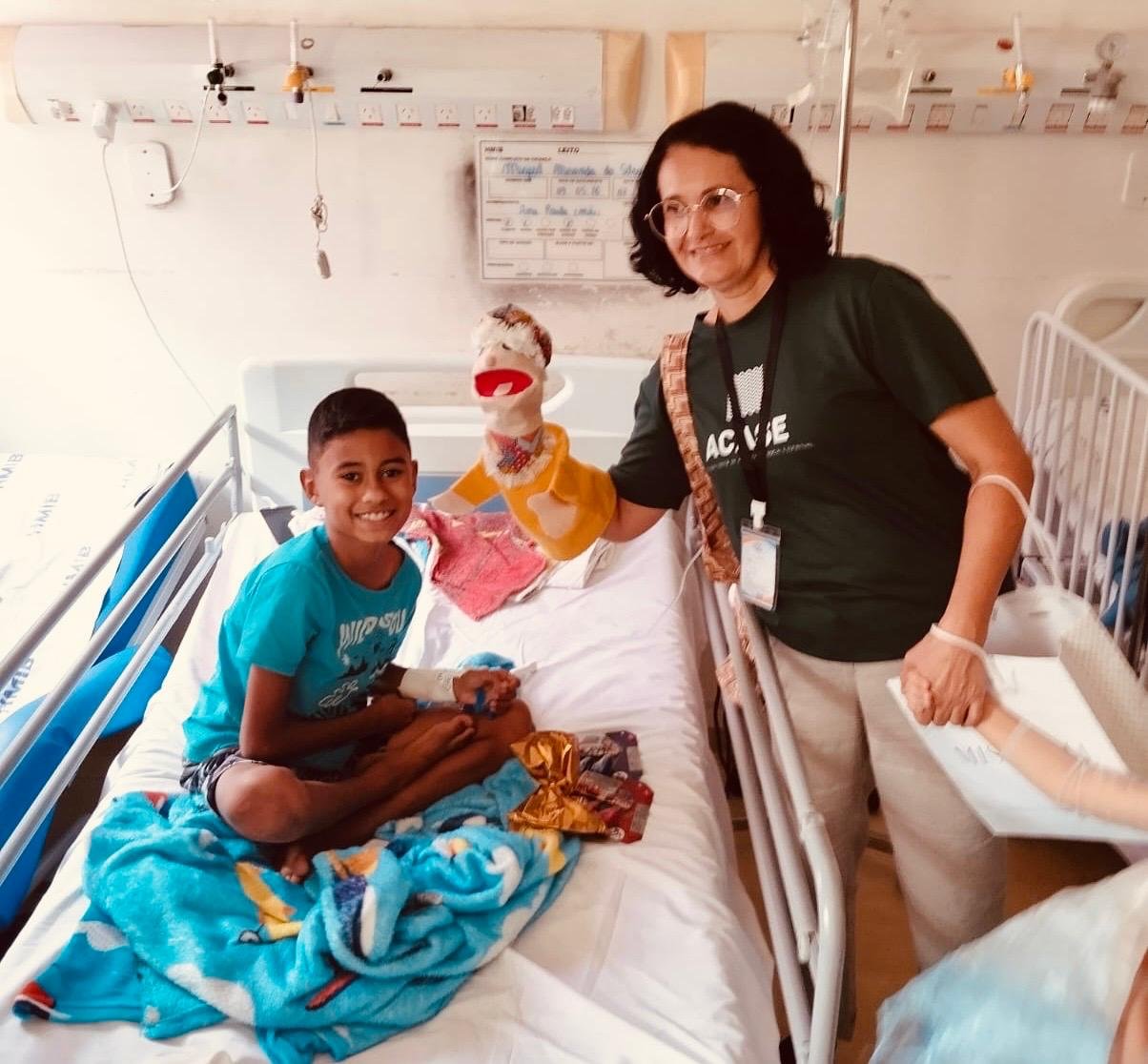 Voluntária da ACASE visita um menino sorridente no leito do hospital.